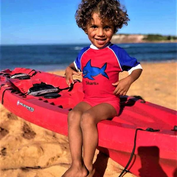 little boy wearing our ozi varmints short sleeve rash vest with a shark design print - red