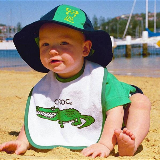 a baby boy wearing an ozi varmints baby bib with white/green colour and a crocodile design printed in the middle