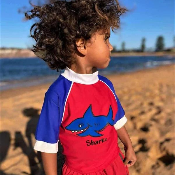little boy wearing our ozi varmints short sleeve rash vest with a shark design print - red