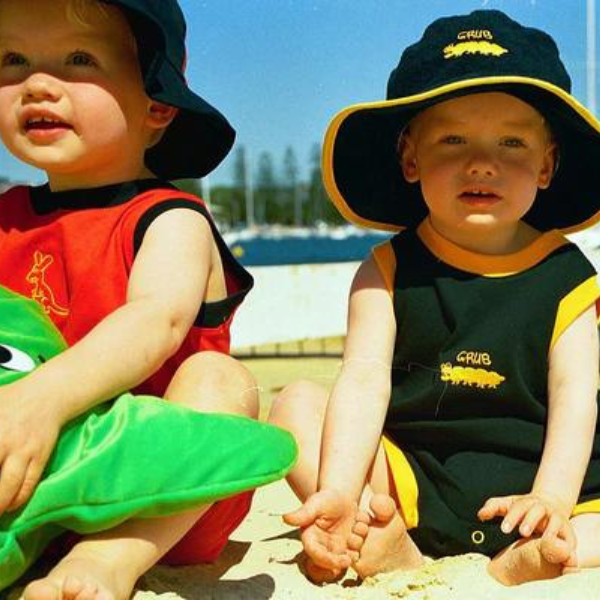 two babies sitting on the beach wearing ozi varmints toweling hat